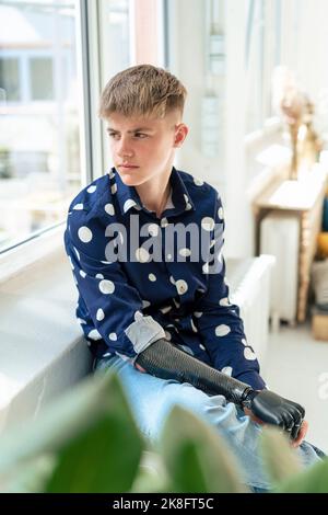 Thoughtful teenage boy with amputated arm looking out through window Stock Photo
