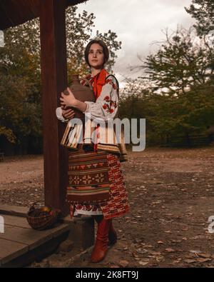 Pensive beautiful young woman dressed traditional ukrainian embroidered clothes holding old crock in her hands looking away. Vintage outfit Stock Photo