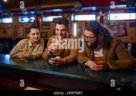 Friends having fun, talking drinking beer and using smartphone Stock Photo