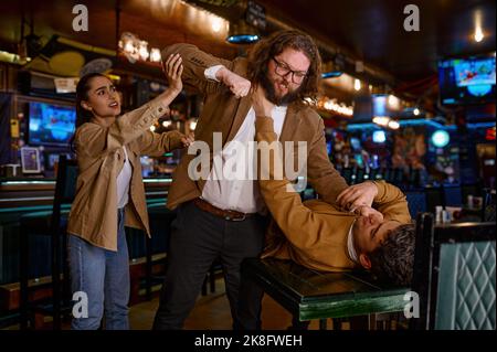 Young woman trying to separate craze mad fighting friends Stock Photo