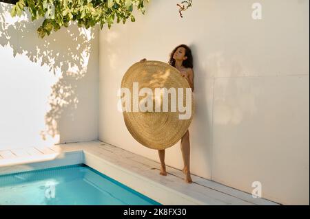 Portrait of fit tanned slim woman holding giant straw hat Stock Photo