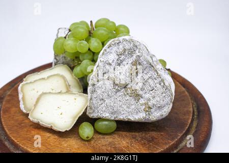 Assorted mouldy blue cheeses goat milk on a wooden chopping board with green grapes. White background. Stock Photo