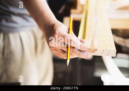 A carpenter measures the planks to assemble the parts and build a wooden table for the customer. Stock Photo