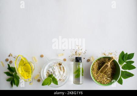 Alternative medicine, herbal extract: jar of oil, bowl with white essence, and stirring. Bowl with ground dry medicinal herbs, green leaves and pills. Stock Photo