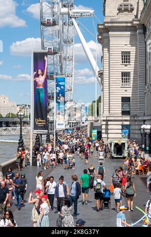 London Eye, Millennium Wheel, beside the South Bank of the River Thames. County Hall building. Madame Tussauds banner. Al fresco diners Stock Photo