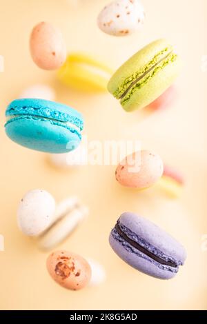 Multicolored flying macaroons and chocolate eggs frozen in the air on blurred beige background. top view, flat lay, close up. Breakfast, morning, conc Stock Photo