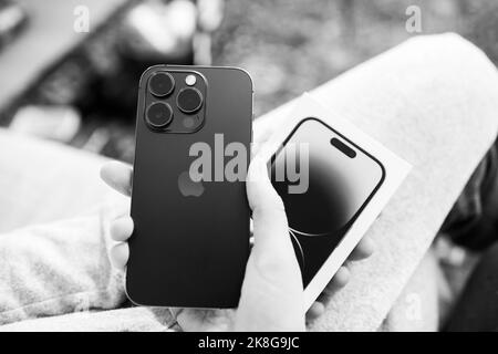 London, United Kingdom - Sep 28, 2022: black and white image POV woman hand holding the package showing newly released iPhone 14 pro by Apple Computers - looking at the triple camera wide ultra-wide and telephoto Stock Photo