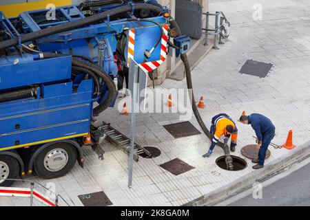 Galicia, Spain; september 30, 2022: Sewerage truck and two workers on street unblocking a sewer with a hosepipe Stock Photo