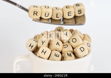 Business concept. Cubes with the image of letters are poured into the cup, above the cup there is a spoon with cubes with the inscription - Rules Stock Photo