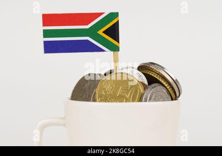 The flag of South Africa sticks out of a cup with coins. Economy and business concept. close-up Stock Photo