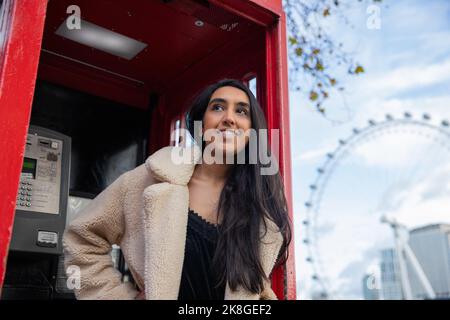 Portrait of a girl in London smiling in a telephone box. Stock Photo