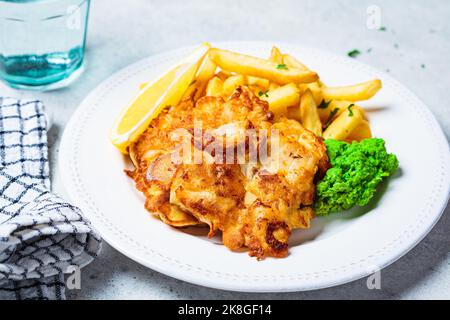 Fish and chips. Cod fish in batter with french fries and mashed green peas on white plate, gray background. English food concept. Stock Photo