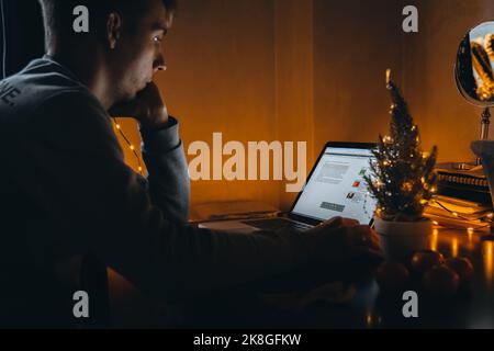 Concentrated freelance business man in typing on computer keyboard while working in home office interior decorated for Christmas holidays, male employ Stock Photo