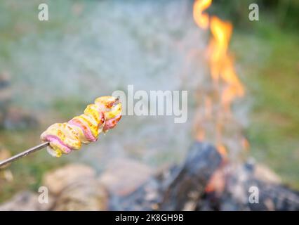 Close-up video of food being grilled over a campfire near a tent at a campsite. Focus on the fire. Marshmallow on fire Stock Photo