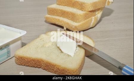 Spreading butter onto toast with knife on wooden board Stock Photo