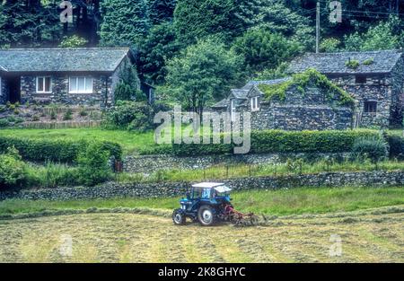 1990s archive image of a Ford 4110 tractor turning or tedding hay at Bridgend in Patterdale in the English Lake District. Stock Photo