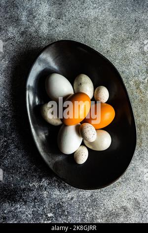 Bowl with multicolor chicken eggs and quail eggs as a spring Easter concept on concrete background Stock Photo
