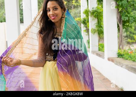 Positive young Indian female in traditional clothes and headscarf smiling and looking at camera in green park Stock Photo