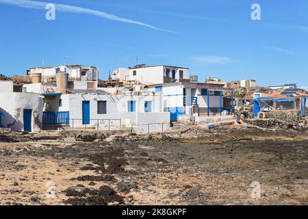 White buildings with blue parts located on volcanic seacoast against blue sky in Fuerteventura, Canary Islands, Spain Stock Photo