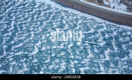 Aerial top view of uneven coast of calm dark sea covered with white snow on cold winter day in Iceland Stock Photo