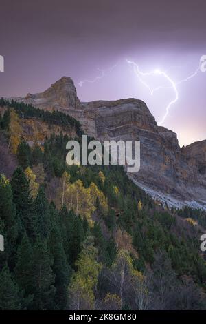 From below rough dramatic landscape of rocky cliff under stormy sky with bright lightnings during sunset Stock Photo