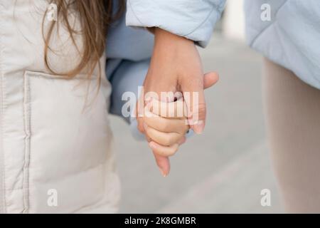 Anonymous mom and daughter in outerwear holding hands while standing on city street in daytime Stock Photo