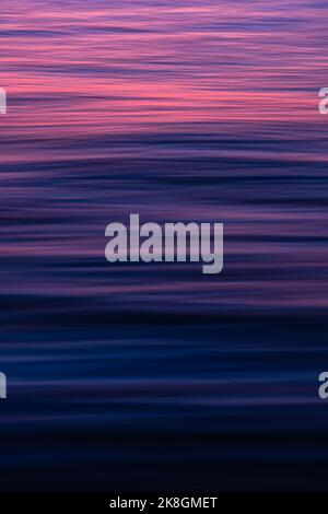 Full frame background of blue sea water rippling and reflecting pink sundown light Stock Photo
