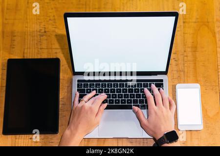 From above anonymous female freelancer browsing on laptop with blank screen near tablet and smartphone while sitting at table in restaurant Stock Photo