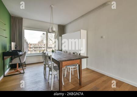big wooden table with chairs near desk with computer close to window in a modern big house. Stock Photo