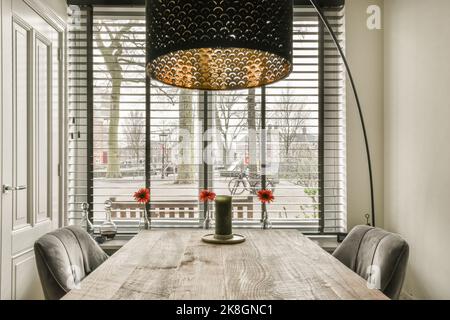 Dining wooden table with decorative elements placed under stylish lamp in apartment with big window Stock Photo