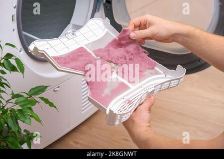 A man holds a dirty dryer filter. A man collects lint, hair, wool from the filter of a drying machine. Red lint on the dryer filter. Dirty filter dryer. Stock Photo
