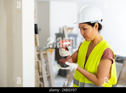 Woman builder using drill to bore hole in wall Stock Photo