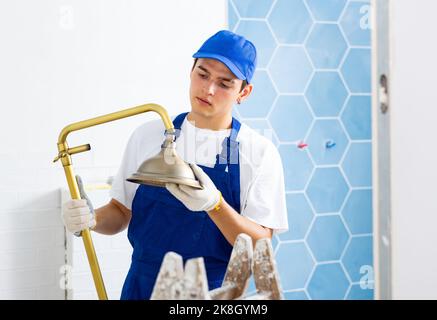 Focused young plumber installing shower in apartment under renovation Stock Photo