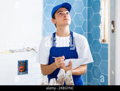 Focused contractor taking notes while planning renovation works in building Stock Photo