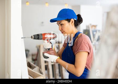 Asian woman construction worker drilling hole in wall Stock Photo