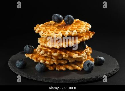 Fresh crispy with a golden crust Belgian waffles with blueberries on a black stone plate on a black background Stock Photo