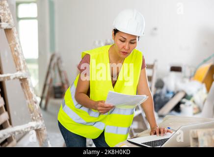 Woman builder checking project documentation and using laptop Stock Photo