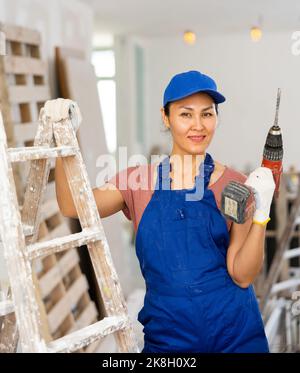 Smiling woman builder holding drill, repair works in apartment Stock Photo