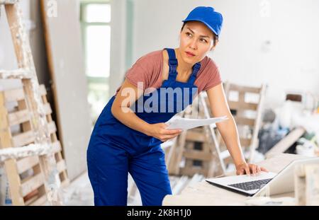 Woman builder checking documentation, using laptop Stock Photo