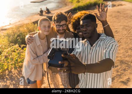 Four beautiful multiracial people of different genders taking a selfie with analog instant camera during shiny sunset at the river. Creation of memories. High quality photo Stock Photo