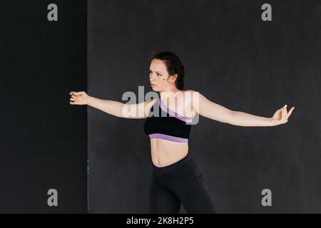 A pretty brunette girl dancing contemporary dance. Dark backgroud. Smooth body movements. Studio portrait of a young sports woman. Femininity concept. Stock Photo