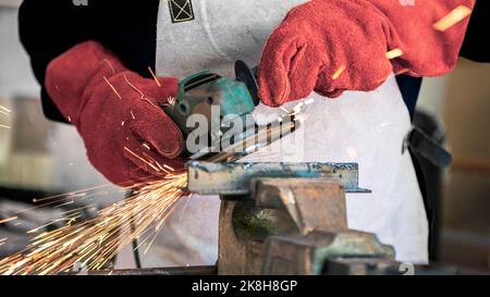 Metal processing with a man using angle grinder to cleaning the steel seam. Locksmith in special clothes and gloves works in production. Sparks in met Stock Photo