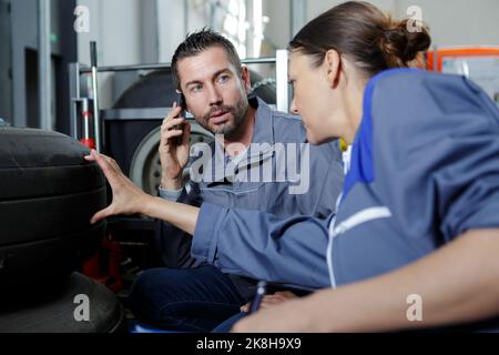 handsome auto mechanic helping a female colleague to chose tyres Stock Photo