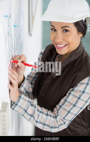 woman wearing a safety helmet writing on a noticeboard Stock Photo