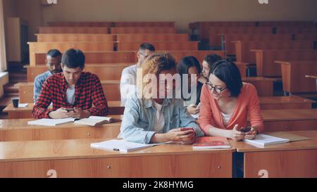 Cheerful students multiethnic group are using smartphones and chatting during break between lectures at university. Modern technology, youth and education concept. Stock Photo
