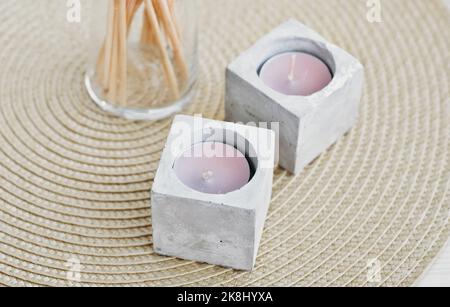 trendy concrete candlesticks with tea candles on wicker table mat. minimal house decor.hand made cement candlesticks Stock Photo
