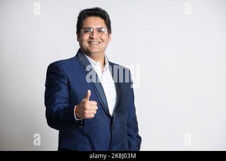 Portrait of a confident young indian business man in a suit do thumbs up isolated on white background. successful asian smiling male ceo of company st Stock Photo