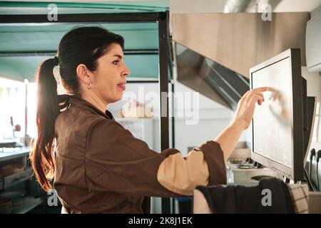 Woman checking the orders on a touch screen while working in a restaurant. Stock Photo