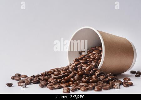 Not all coffees are created equal. Studio shot of a tipped over paper cup filled with coffee beans against a grey background. Stock Photo