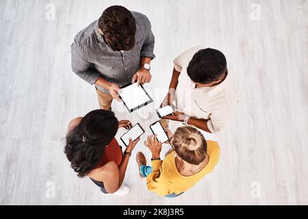 Modern tools are needed to adapt to the market. High angle shot of a group of young designers using digital devices in synchronicity in an office. Stock Photo